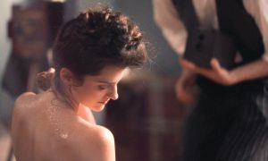 Marie de Régnier interprétée par Noémie Merlant nue assise à l'intérieur d'une bassine d'eau se lave sensuellement avec une éponge humide devant l'objectif de son amant photographe qui réalise des photos érotiques dans le film Curiosa en 2019