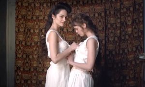 Marie de Régnier incarnée par Noémie Merlant et Louise de Heredia incarnée par Mathilde Warnier s'apprêtent à faire l'amour ensemble à leur mari et amant qu'elles se partagent sans tabous dans le film Curiosa en 2019