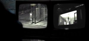 Le Maître du jeu de l'escape game surveille avec une caméra vidéo la jeune femme toute nue au milieu d'une rue en gardant ainsi le contrôle sur la jeune captive qu'il vient de libérer dans le film Escape Room en 2017