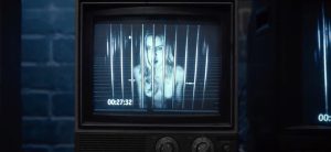 La jeune femme nue encagée subit une exhibition publique permanente car les images de son enfermement à l'intérieur de sa cage minuscule sont retransmises en direct sur des moniteurs vidéo afin que les autres joueurs de l'escape game puissent bien observer la nudité totale de la jolie captive dans le film Escape Room en 2017