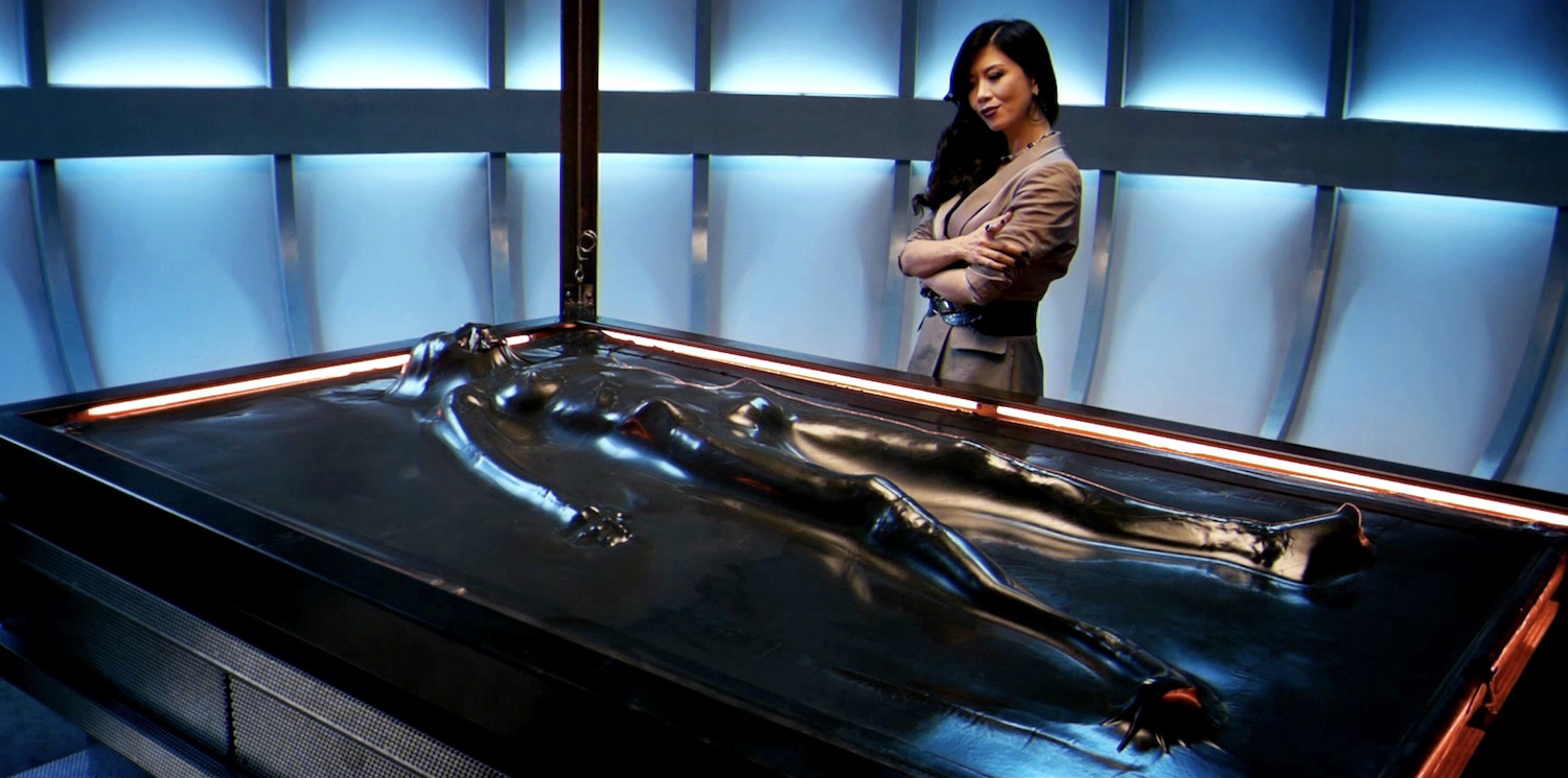 La jeune soumise nue emprisonnée entre les deux draps de latex d'un vacuum bed sous l'autorité altière de sa Maîtresse lesbienne dans le film Les Nuits rouges du bourreau de Jade en 2009