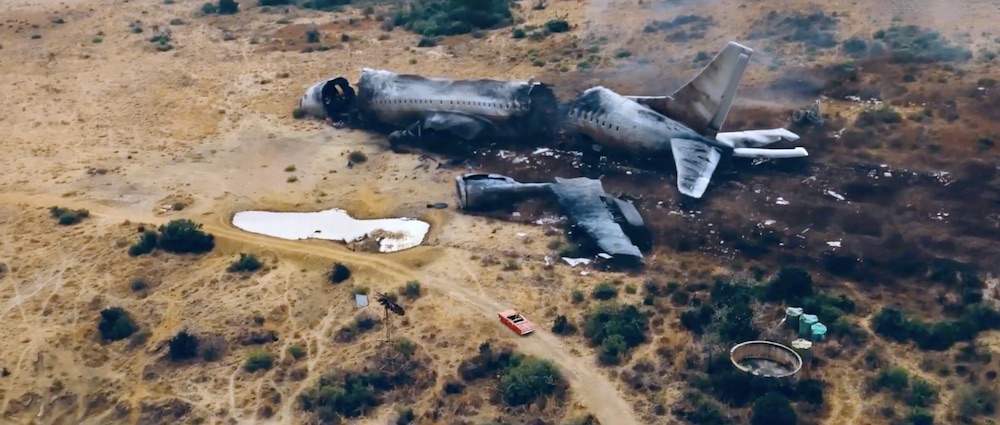 La voiture décapotable de Bo et Nadia s'approche de la carcasse d'un avion de ligne civil qui s'est écrasé au sol durant l'invasion extra-terrestre dans le film Revolt en 2017